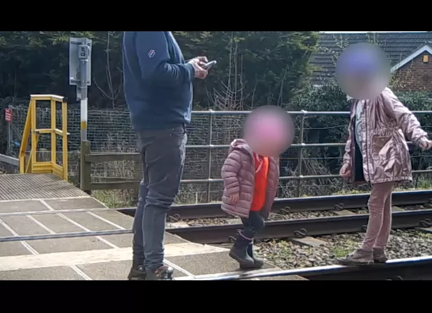 Dad seen on security footage allowing two kids to play on active train tracks.