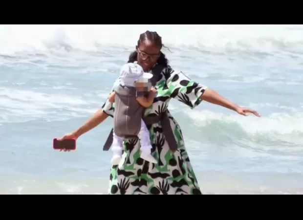 Dance competition celebrity enamored with 7-month-old daughter, twirls and sways with her on the shore.