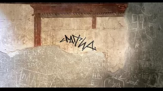 Tourist vandalizes ancient Roman building by writing on it with marker.