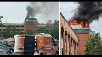 A shopping center is on fire, with large clouds of smoke billowing into the air.
