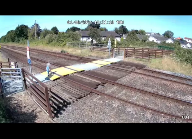 Small child walks out onto crossing by themselves, narrowly missing a train.