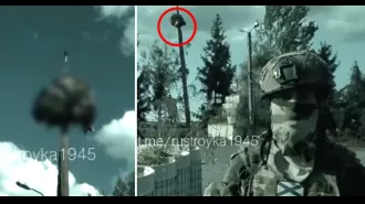 A Russian soldier holds up the decapitated head of a Ukrainian soldier on top of a stake.