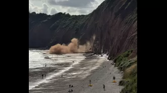 People laying on beach run into ocean to get away from falling cliff.