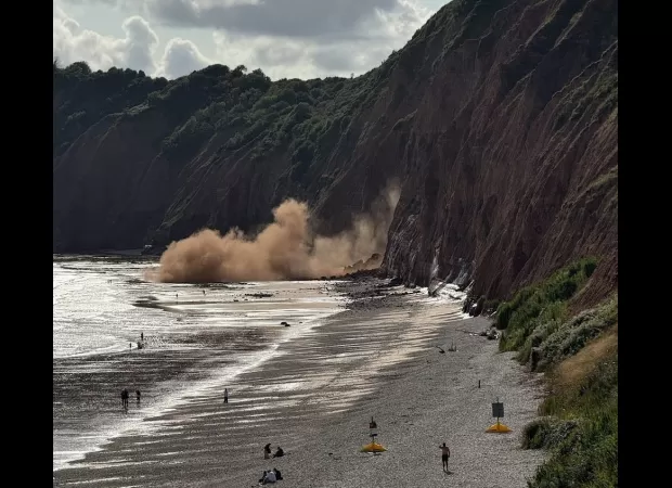 People laying on beach run into ocean to get away from falling cliff.