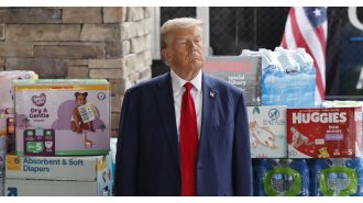 Trump promoting Hurricane Helene aid amidst a backdrop of toilet paper and diapers.