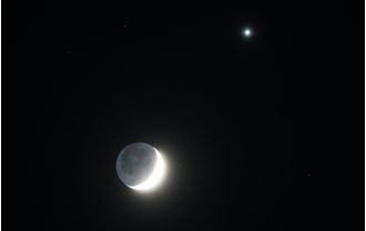 The Moon's crescent shape is illuminated by the bright light of Venus.