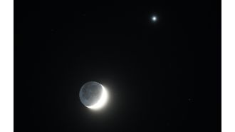 The Moon's crescent shape is illuminated by the bright light of Venus.